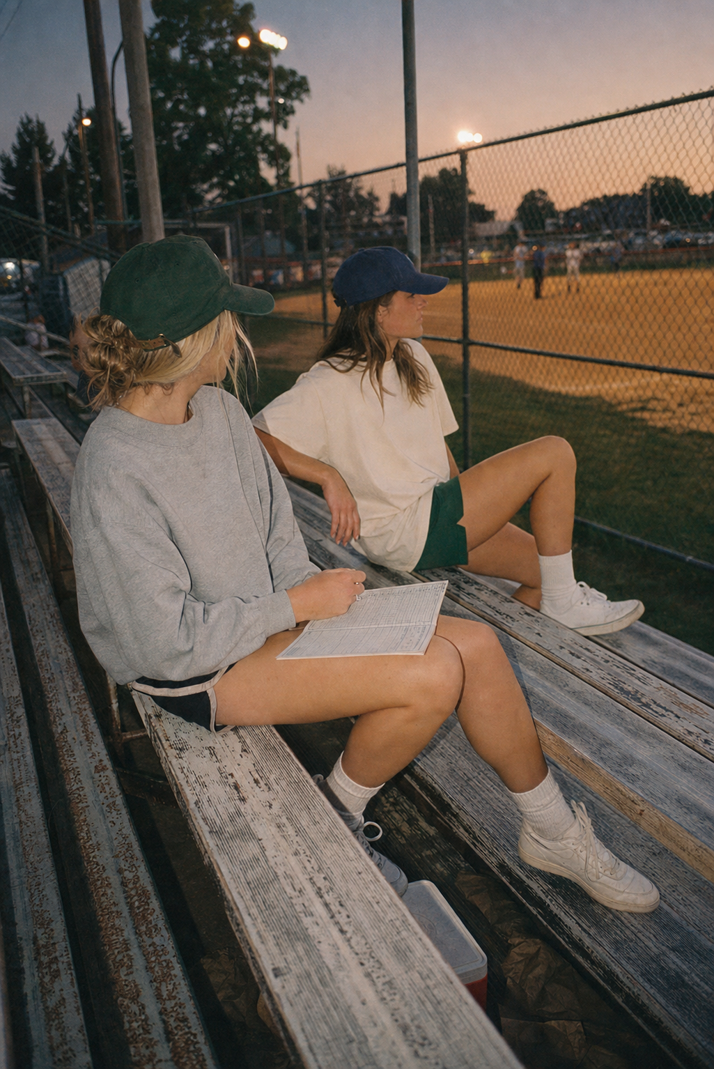 Two friends keeping score on the bleachers at sunset